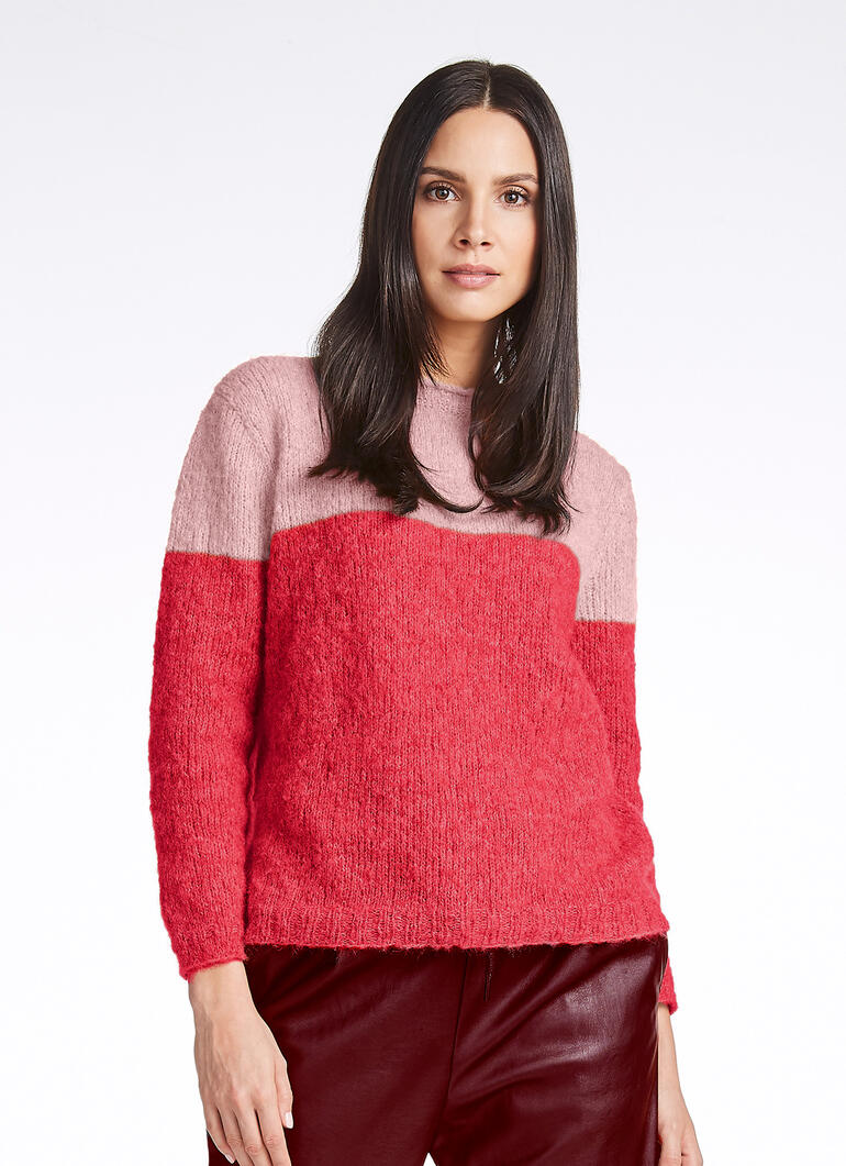 Frau in einem Farbblock-Pullover in Rosa- und Rottönen, lächelnd in die Kamera.