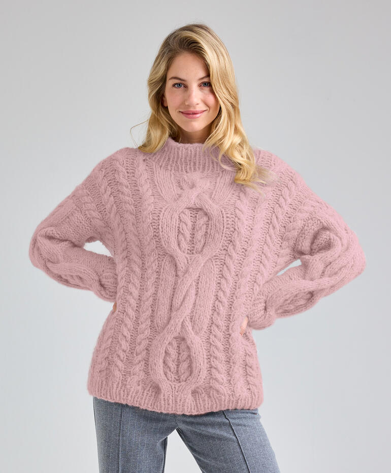 Frau in einem strukturierten, rosa Pullover mit Zopfdesign, posiert freundlich.