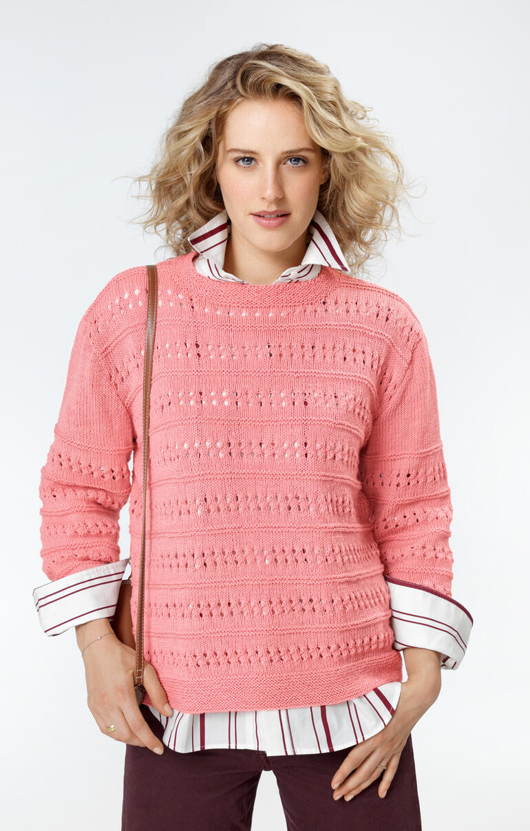 Frau in einem rosa Pullover mit Lochmuster, kombiniert mit Hemd und Tasche.