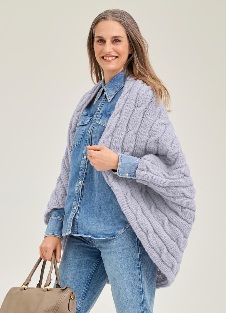 Frau in grauem, dickem Ärmelschal aus Wollmaterial, trägt eine Jeansjacke.