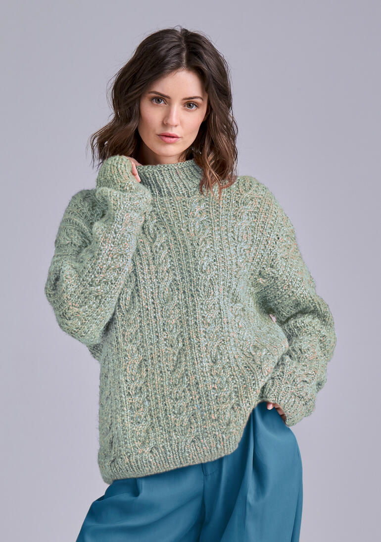 Frau in einem grünen, strukturierten Pullover, schaut wahrhaftig in die Kamera.