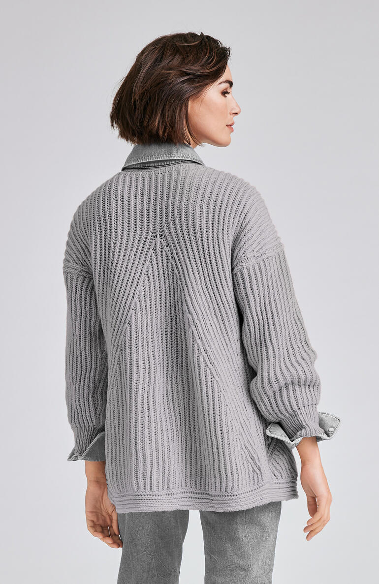 Frau trägt eine graue Jacke aus Merino-Wolle, betrachtet einen Wald.