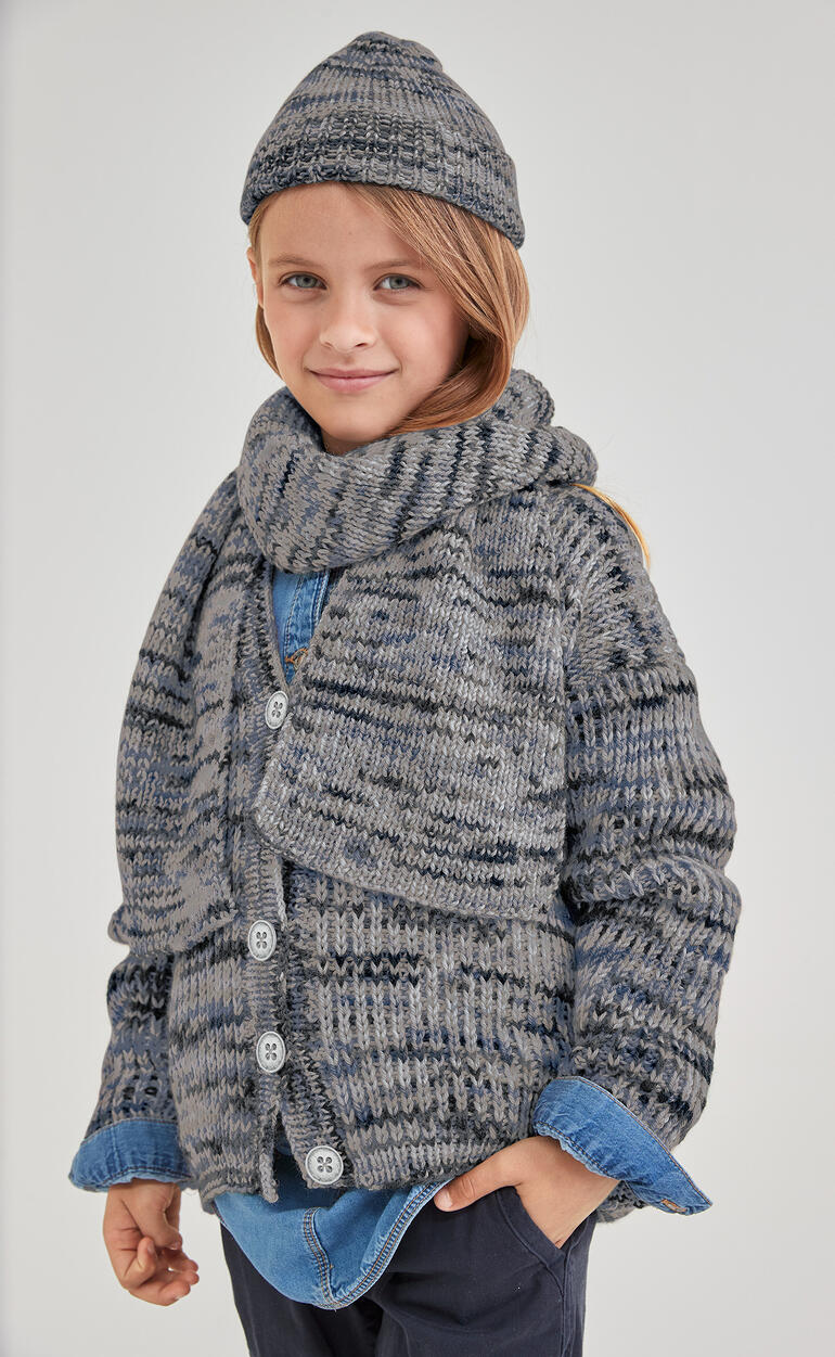 Jungenkind in gestreiftem Mützen und Schal aus Merino-Print, lächelnd.