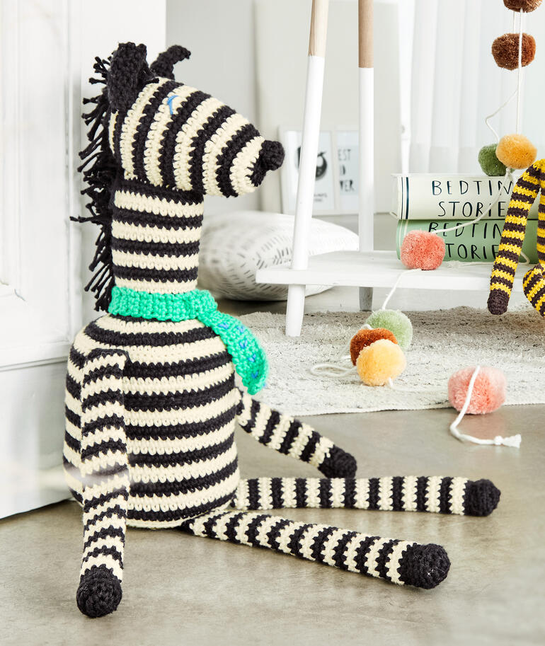 Häkelzebra ‚Zack‘ aus Cotonara, sitzend mit türkisfarbener Schärpe.