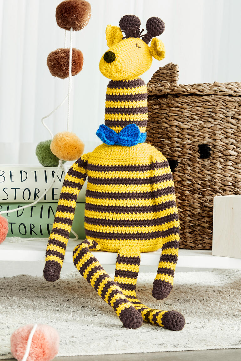 Häkelgiraffe ‚Gordon‘ aus Cotonara und Poco, sitzend mit blauer Schleife.