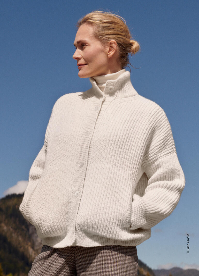 Frau trägt einen weißen Cardigan aus Alta Moda Alpaca von Lana Grossa unter blauem Himmel.