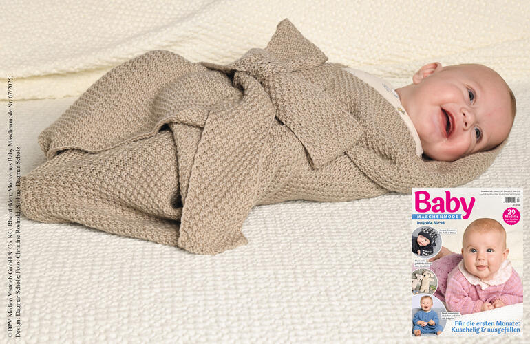 Lächelndes Baby in einem Pucktuch aus Nuovo Merino auf einem weißen Strickstück