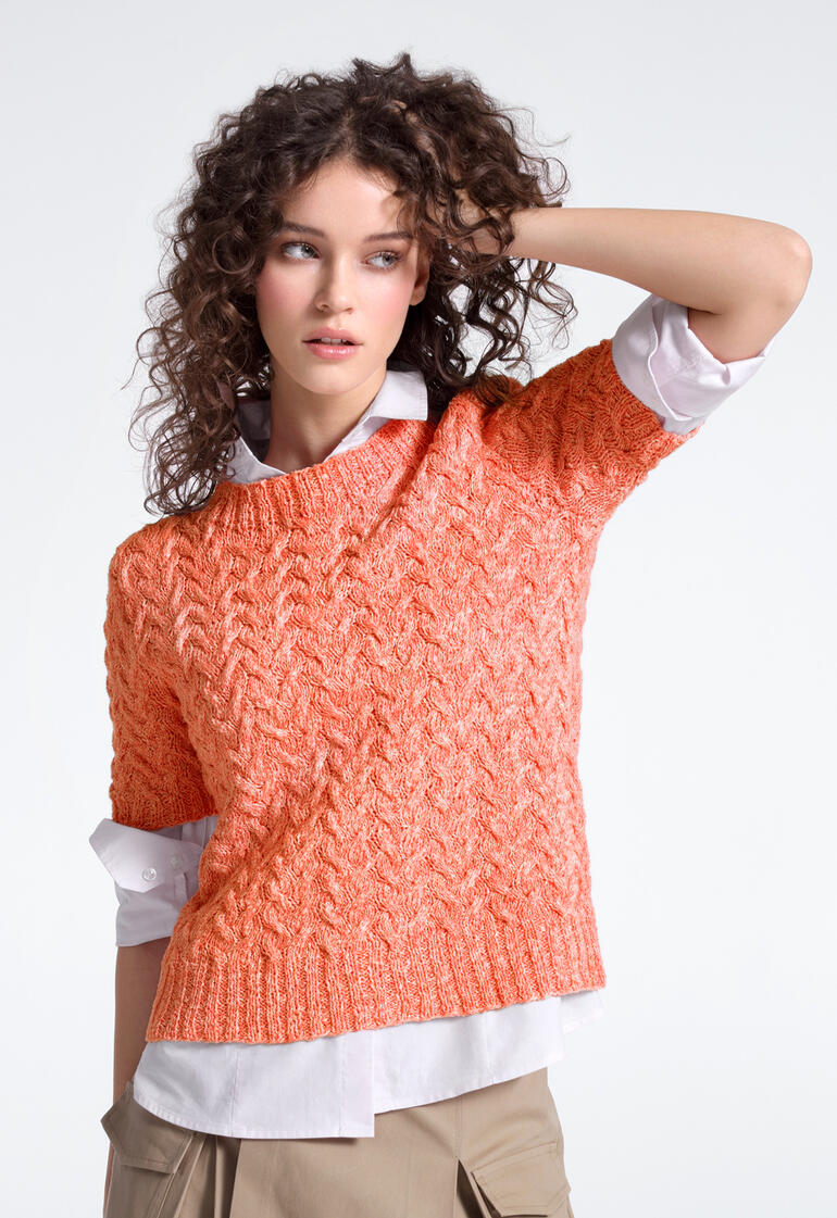 Frau in orangefarbenem Pullover aus Contrato posiert modisch.