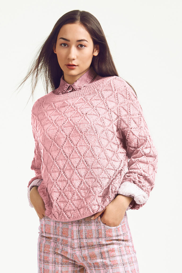 Frau mit rosa Pullover aus Seidana, trägt ein Hemd darunter, vor neutralem Hintergrund.