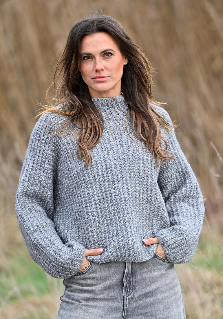 Grauer Pullover mit hohem Kragen, Modell posiert in freier Natur.