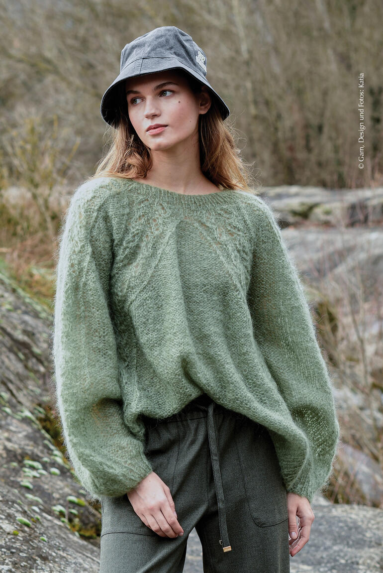 Grüner Pullover aus Ingenua, Modell mit Hut im Freien.