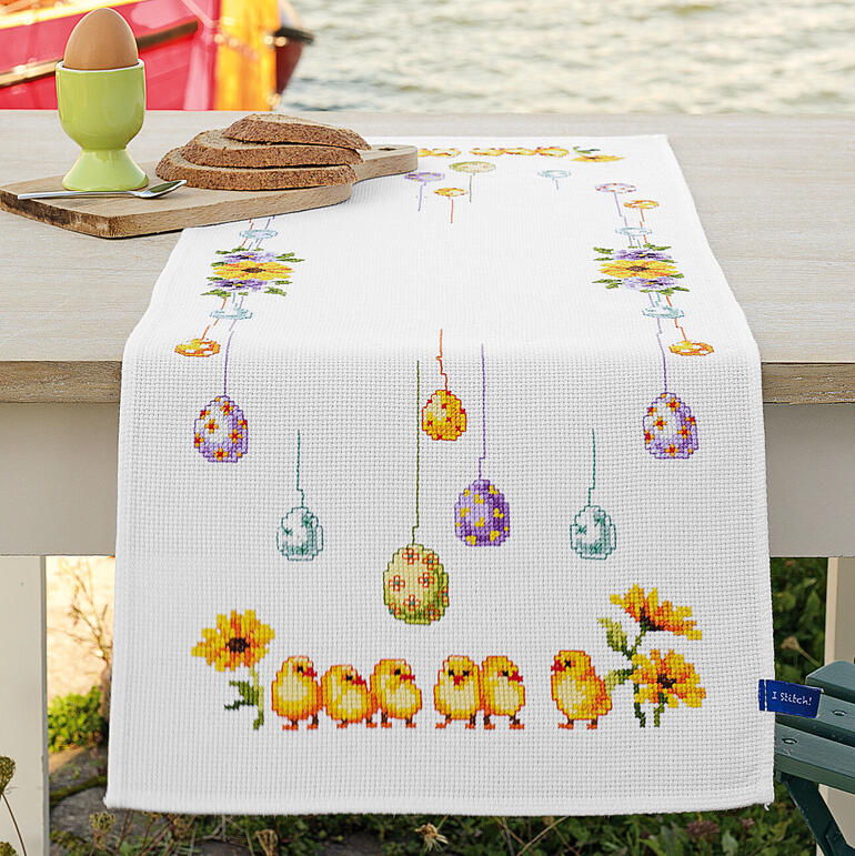 Aida-Tischläufer mit Küken und Ostereiern auf weißem Grund.