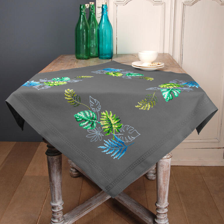 Tischdecke mit bunten botanischen Blättern auf einem Holztisch.