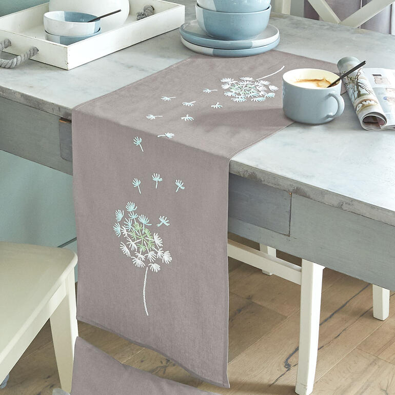 Tischläufer mit Pusteblumenmotiven auf einem gedeckten Tisch.