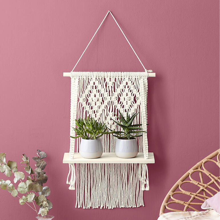 Makramee-Hängeregal mit Pflanzen auf rosa Wand
