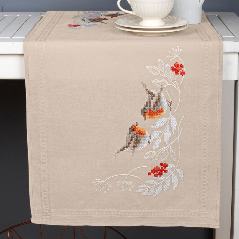Tischläufer mit einem Rotkehlchen und winterlichen Motiven auf beigefarbenem Stoff.