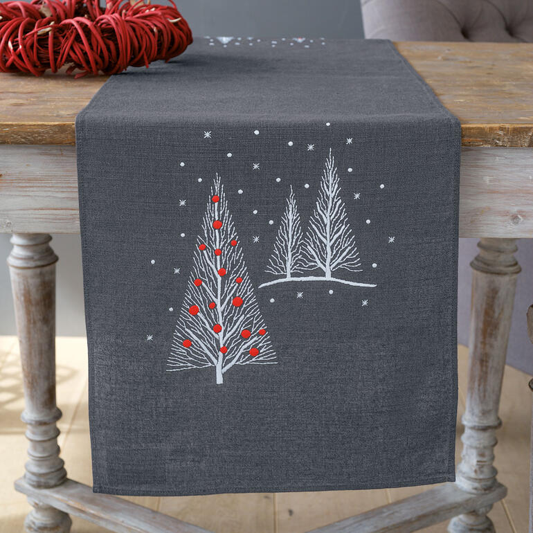 Tischläufer mit Weihnachtsbäumen und roten Kugeln auf einem grauen Tisch.