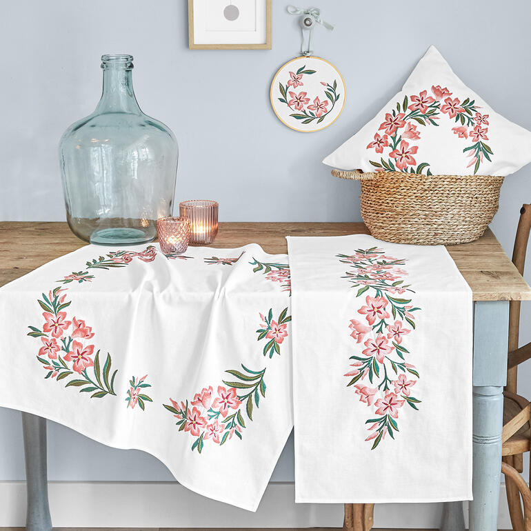 Tischdecke, Kissen und Stickrahmen mit Oleanderdesign auf einem Tisch.