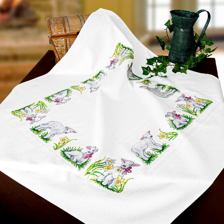 Tischdecke mit gestickten Lämmchen umrahmt von bunten Blumen.