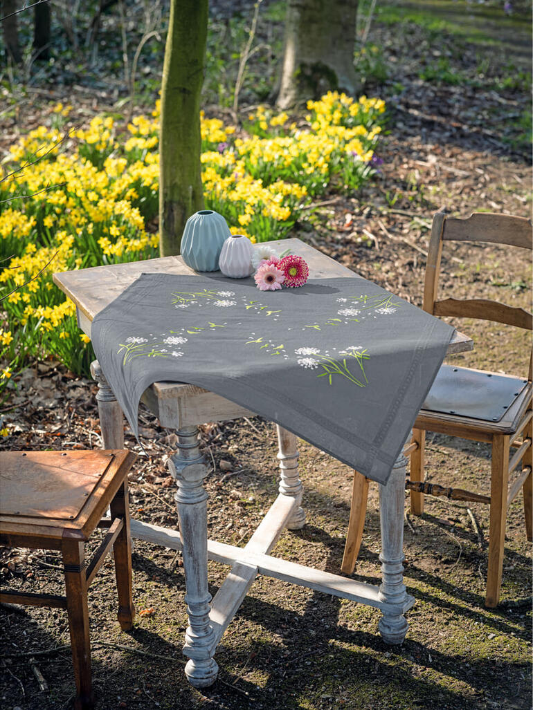 Tischdecke mit Pusteblumenmotiven auf einem Holztisch im Freien.