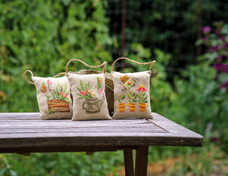 Drei Deko-Kissen im Garten-II-Design, illustriert mit Pflanzenmotiven auf einem Tisch.