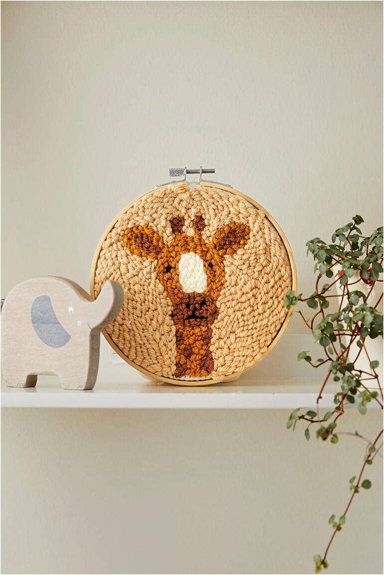 Punch Needle Set mit Giraffenmotiv in einem Rahmen auf einem Regal.