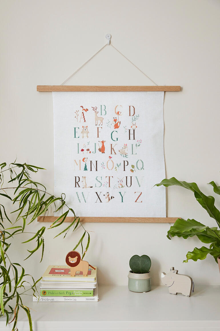 Stickbild mit Tieren und Alphabet an einer Wand aufgehängt.