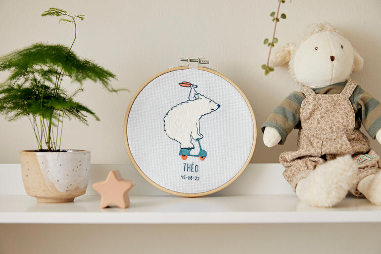 Stickbild mit einem Polarbären und Spielzeug auf einem Tisch.