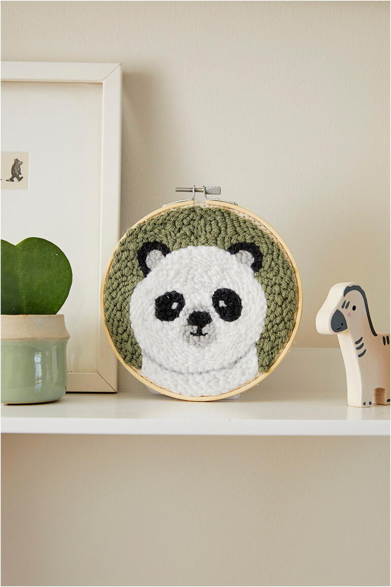 Rundes Stickformat mit Panda-Gesicht auf grünem Hintergrund, präsentiert auf einem Regal.