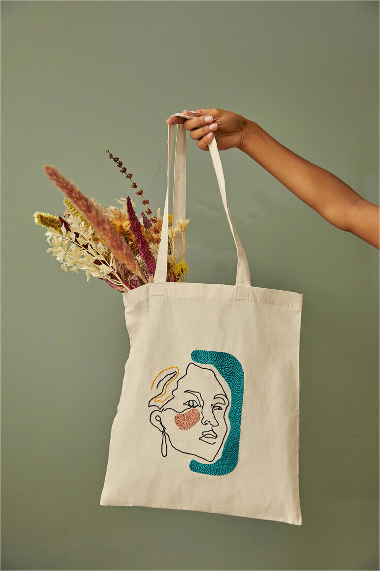 Tasche mit einer linearen Kunstzeichnung einer Frau und getrockneten Blumen in der Hand.