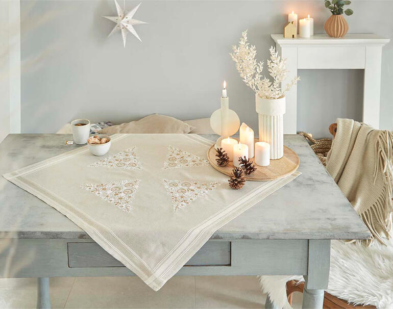 Tischdecke mit Kunstdekor und Kerzen auf einem festlich gedeckten Tisch.