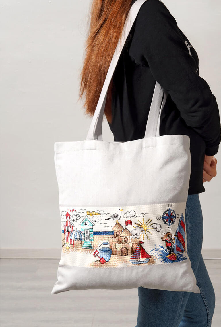 Baumwolltasche mit gesticktem Strandmotiv, getragen von einer Frau.