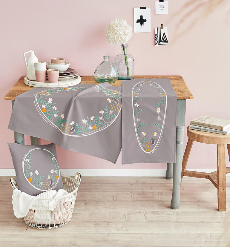 Tischset und Kissen mit floralen Mustern auf einem Holzstisch.