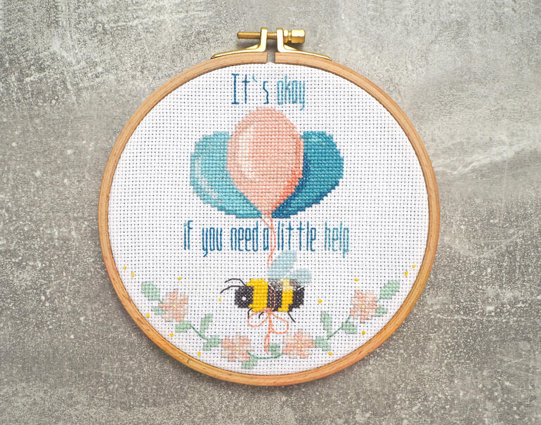 Kreuzstichbild mit einem Bienenmotiv und Luftballons, fröhliche Farben.