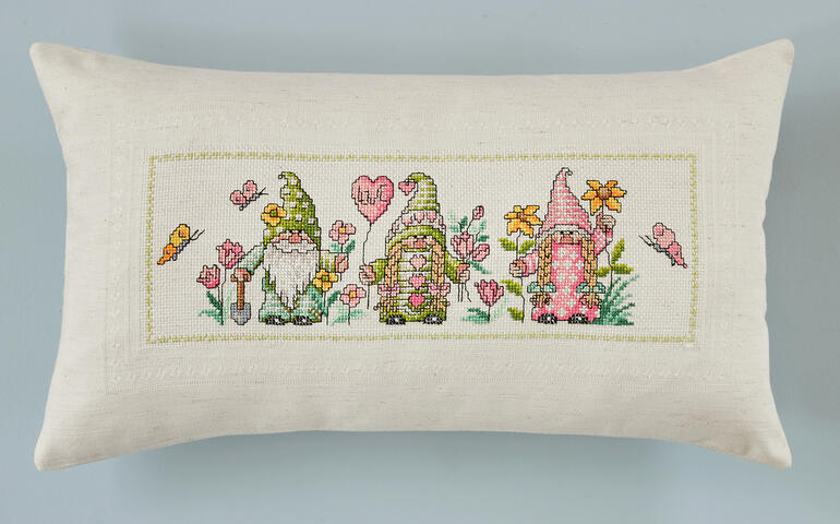 Kissenhülle mit Wichtelmotiven im Frühjahr, umgeben von Blumen und Schmetterlingen.
