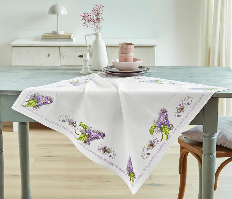 Aida-Tischdecke mit lila Fliederblüten auf einem weißen Untergrund.