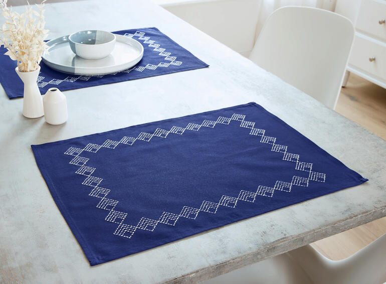 Zwei dunkelblaue Platzdeckchen mit geometrischem Muster auf einem Tisch.