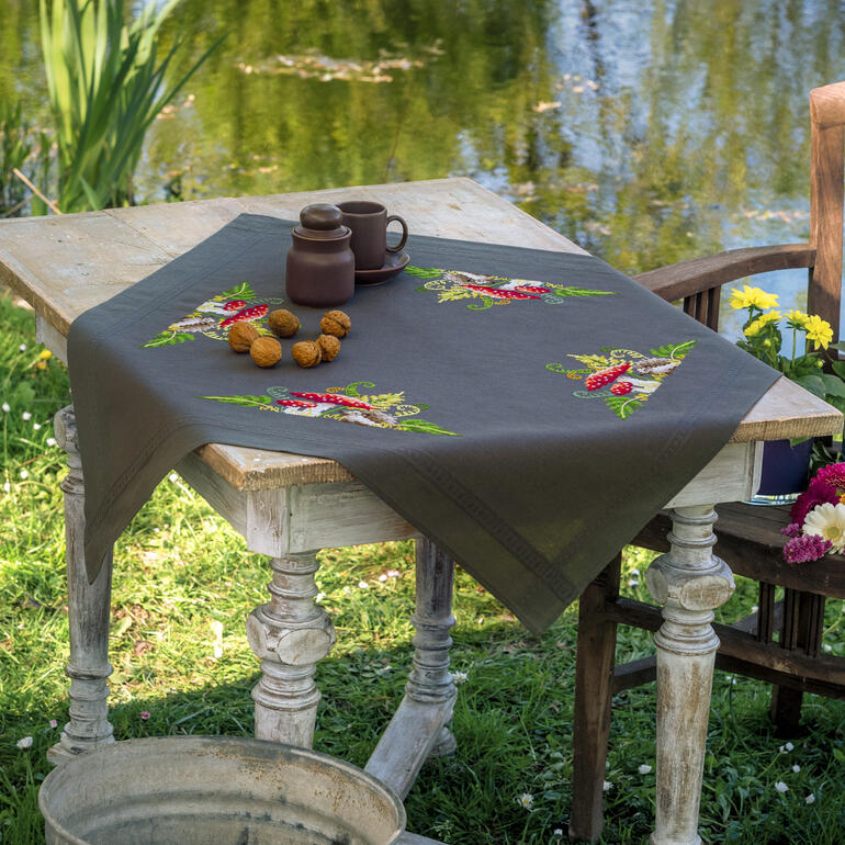 Tischdecke mit Igeln und Farnen auf einem holzigen Tisch am Teich.