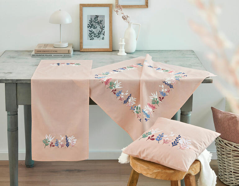 Stilvolles Tischsetting mit einer bestickten Tischdecke und Kissen im modernen Design.