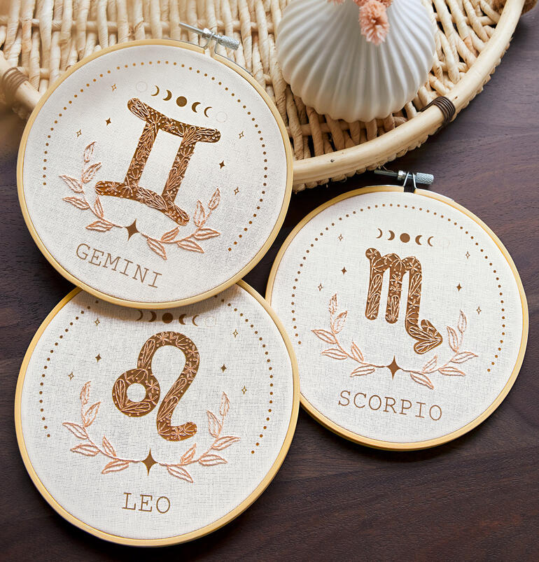 Drei Muster von minimalistischer Tierkreis-Stickerei auf einem Tisch.