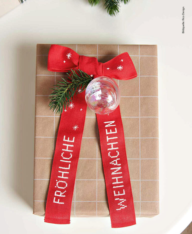 Geschenk eingepackt mit roter Schleife und Weihnachtsdekoration.