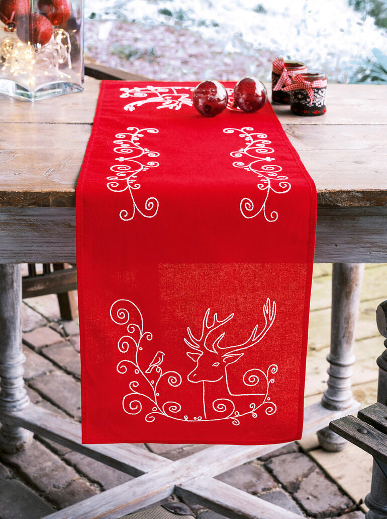 Tischläufer in Rot mit einem Elch und einem Vogel, dekoriert mit Weihnachtskugeln.