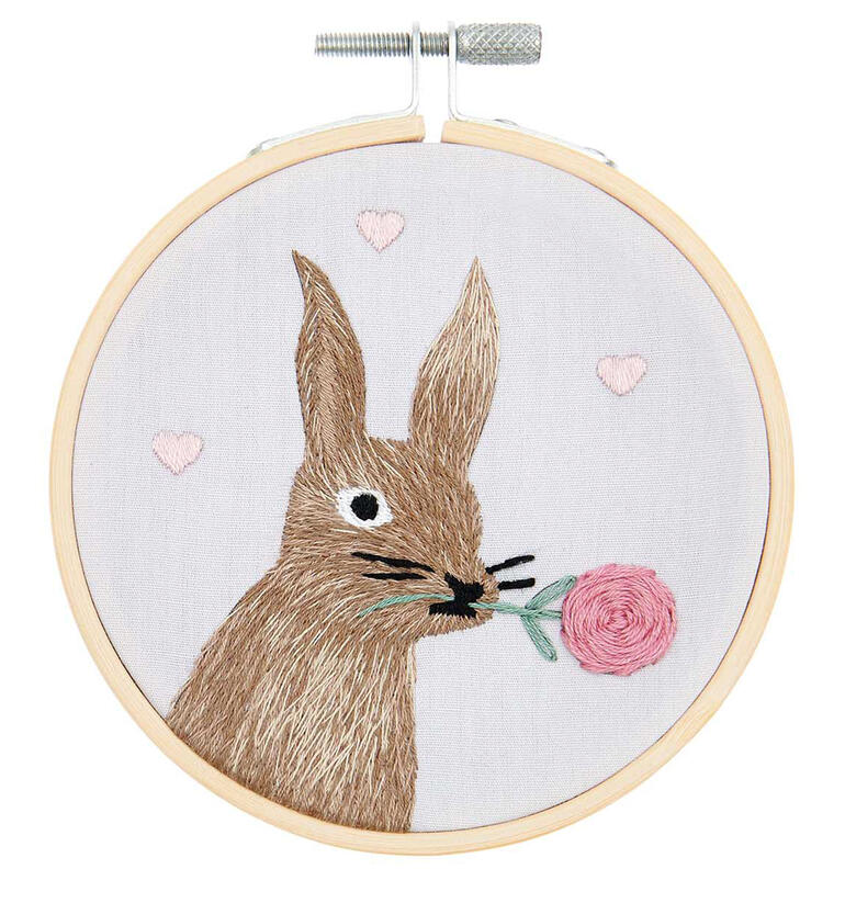 Stickbild eines Hasen mit einer Blume, umgeben von Herzen, in einem Stickrahmen.